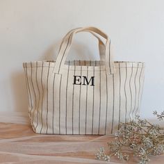 a white and black striped tote bag sitting on top of a wooden table next to a plant