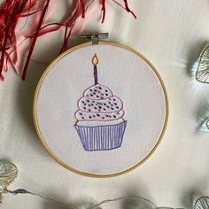 a cupcake with a candle in it is embroidered onto a white fabric and surrounded by red streamers