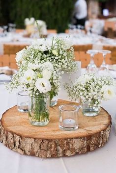 white flowers in vases on a wood slice at a wedding reception with candles and wine glasses