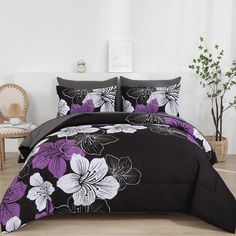 a black and white bed with purple flowers on the comforter, next to a potted plant