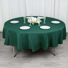 a green table cloth with white plates and flowers on it, in front of a curtain