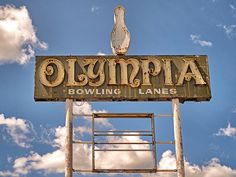 an old sign that says olympia bowling lanes on it's side with the sky in the background