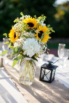 a vase filled with white and yellow flowers on top of a table next to a lantern