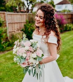 a woman in a white dress holding a bouquet of flowers and smiling at the camera