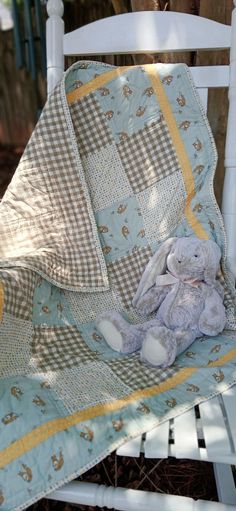 a teddy bear sitting on top of a white chair under a blanket with yellow trim