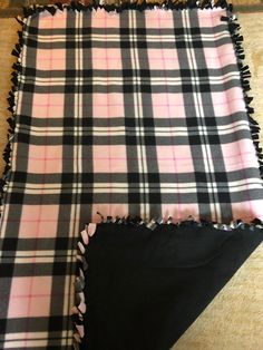 two pieces of black and pink plaid fabric with fringes on the edges, laying next to each other