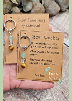 the best teacher keychain is shown in front of a card with two charms on it