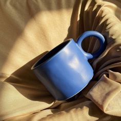 a blue mug sitting on top of a bed next to a brown blanket and pillow