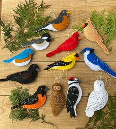 small felt bird ornaments are arranged on a wooden table with greenery and pine branches