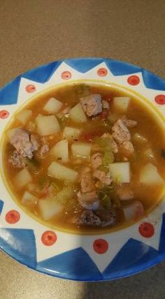 a bowl of soup with meat and potatoes on a blue and white plate sitting on a brown table