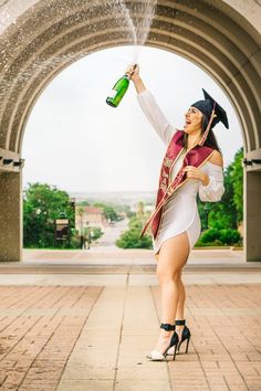 a woman in a graduation gown is holding a bottle and spraying water on her head