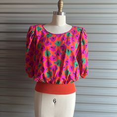 Bright floral silk in Orange pink and green. Has a knit band at waist and sleeves. Has moderate shoulder pads and puffy sleeves. Tags: Emmanuel Ungaro / size 12  100% Silk/ Fabric made in Italy Nice condition, no flaws c1980s also have a lime green with navy and red flowers Measures / meant to be worn loose shoulders 15" Bust 40" Waist Band (stretchy) up to 30" + Length 21 1/2" Pink Fitted Blouse With Balloon Sleeves, Multicolor Fitted Blouse With Balloon Sleeves, Fitted Multicolor Blouse With Balloon Sleeves, Fitted Multicolor Balloon Sleeve Blouse, Vintage Pink Puff Sleeve Top, Multicolor Fitted Blouse With Puff Sleeves, Fitted Multicolor Puff Sleeve Blouse, Pink Fitted Blouse With Blouson Sleeves, Emmanuel Ungaro