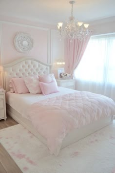 a white bed with pink comforter and pillows in front of a chandelier