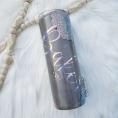 a silver tumbler sitting on top of a white fur covered floor next to a wooden beaded necklace