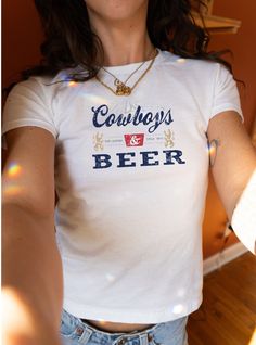 Saddle up for style with our 'Cowboys & Beer' Women's Baby Tee, inspired by the timeless charm of the Old West. This vintage-style tee captures the essence of cowboy culture and the classic enjoyment of a well-deserved beer. With its eye-catching distressed graphic, it evokes the nostalgia of the legendary year 1873. Crafted from the reliable comfort of the Gildan 5000B, this shirt is tailored to fit the modern cowgirl. It's not just apparel--it's a tribute to the stories and the history that sh Vintage Graphic Print Tops For Game Day, Vintage Logo Print Top For Game Day, Fitted Letter Print T-shirt For Game Day, Fitted Cotton T-shirt For Game Day, Vintage Slogan Tops For Fan Merchandise, Vintage Fitted T-shirt With Logo Print, Fitted Vintage T-shirt With Logo Print, Vintage Unisex Text Print Tops, Vintage Text Print Unisex Tops