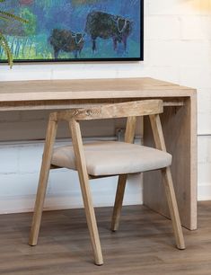 a wooden desk and chair in front of a wall with a cow painting on it