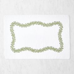 a white place mat with green vines on the edge and a square shape in the middle