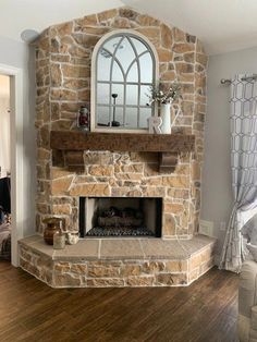 a living room with a stone fireplace and arched window above the mantel, along with hardwood flooring