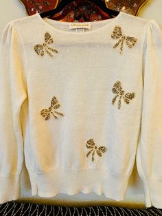 "A beautiful, creamy, super soft, knitted sweater! Features adorable, gold, silver and cream sequined, bows all over! A great way to add a feminine touch to any outfit!  In good vintage condition!  No noticeable stains. Some loose threading and normal vintage wear (see photos) Tag says: no tag/fits like a S Label: Vivanti Made in the U.S.A. Measurements taken while lying flat: Pit to pit: 17\" Shoulder to shoulder: 14\" Top to bottom: 20 1/2\" Sleeve length: 21\"" Photo Tag, Sequin Bow, Gold Flakes, White Sweater, Vintage Knitting, Vintage Wear, Knitted Sweater, Women Pullover, Pullover Sweaters