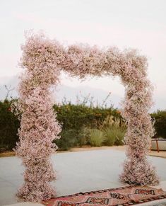 an arch made out of pink flowers in the middle of a cement area with a rug underneath it