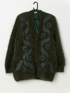 80s vintage fluffy forest green cardigan coat with leather appliqué. This 1980s cardigan coat in forest green features beautiful leather geometric appliqués on the front, a full length button closure, is fully lined and has shoulder pads. Made from a heavyweight mohair blend with a synthetic lining. Our recommended size: Medium to large Label says: No size label Condition: Good* Some light wear on the leather. Please see last image (not colour accurate) Material: 80% mohair, 20% acrylic Lining: Vintage Fall Sweater Coat With Buttons, Green Wool Cardigan For Spring, Green Wool Sweater Coat For Winter, Green Wool Sweater Coat For Fall, Green Wool Winter Cardigan, Vintage Green Cardigan For Fall, Green Vintage Cardigan With Buttons, Vintage Green Winter Outerwear, Vintage Green Outerwear For Fall