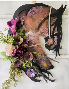 a horse mask with flowers and feathers on the side of a wall next to a flower bouquet