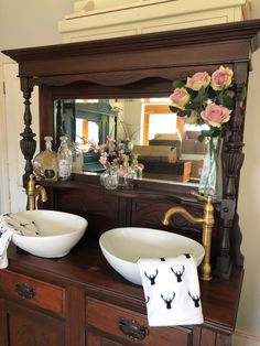 two white bowls sitting on top of a wooden dresser next to a vase with flowers