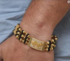 The Mahadev Design Gold Plated Rudraksha Bracelet is a timeless accessory for men. Crafted from brass and plated with gold, this textured design features diamond etching, a shining Rudraksha bead, and a black-hued bracelet for a spiritual yet stylish look. 100% Hid_Reg_Plating ensures lasting shine and durability. Bracelet Dimension Height:20 cm (7.87 inch) Width:17 mm (1.7 cm) Depth:3 mm (0.3 cm) Other Specification Weight:20 Gram Size:Fixed Lock Type:Fold Over / Flap Over Color:Golden, Black M Hand Set Bracelets For Puja During Diwali, Cutdana Bracelets For Puja And Navratri, Adjustable Bollywood Style Bracelet Hand Set, Adjustable Traditional Bracelets For Rituals, Temple Jewelry Style Bracelets With Cutdana For Gift, Navratri Puja Bracelets, Bollywood Style Bracelets For Navratri Rituals, Adjustable Gold Beaded Bracelets For Rituals, Bollywood Cutdana Bracelets For Puja