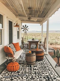 a porch with an orange and black rug on the floor next to two wooden barrels