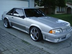 a silver sports car parked in front of a house with a garage door behind it