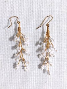 two pairs of gold and white beaded earrings on a white surface with beads hanging from them