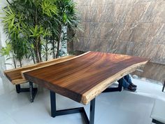 a wooden table sitting next to a plant in a room with white tile flooring