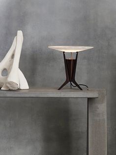 a table with two sculptures on it and a lamp next to it in front of a gray wall