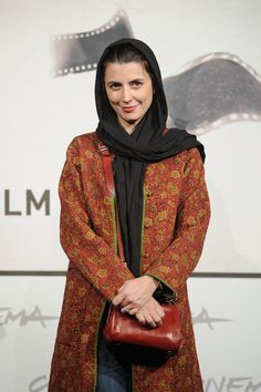 a woman standing in front of a camera holding a purse