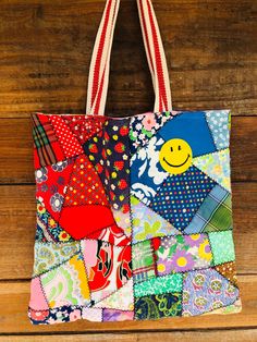 a multicolored patchwork tote bag hanging on a wooden wall with a smiley face painted on it