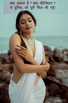 a woman in white sari standing next to the ocean with her arms crossed and eyes closed