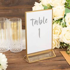 a table number is placed on top of a wooden table next to glasses and flowers