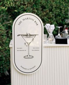 the martini bar is set up outside in front of some trees and shrubbery with glasses on it