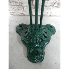 a green vase sitting on top of a cement floor next to a brick wall with holes in it