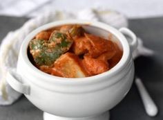 a white bowl filled with food on top of a gray tablecloth next to a spoon