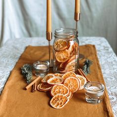 orange slices and cinnamon sticks are on a table with two candles in front of them