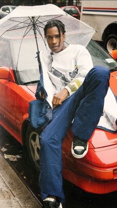 a man sitting on top of a red car holding an umbrella