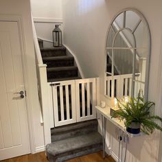 an entryway with stairs, mirror and potted plant on the table next to it