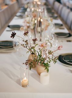 the table is set with candles and flowers in vases on each side, along with other place settings