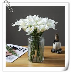 white flowers in a glass vase on a table next to a cat figurine