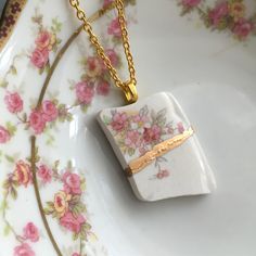 a white plate with pink flowers on it and a gold chain hanging from the edge