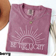 *If you would like a colour or size that is not listed, please contact us. Spread positivity and faith with the Be The Light Matthew 5:14 Shirt! Inspired by the powerful biblical verse, this shirt encourages you to be a guiding light in the world, radiating kindness and love. Perfect for church gatherings, spiritual events, or everyday wear, this shirt is a beautiful reminder of your faith and the impact you can have on others.  🎨 Design Highlights: Elegant "Be The Light" text with Matthew 5:14 Spiritual Event, Matthew 5, Plus Size Shirt, Bible Verse Shirt, Be The Light, Guiding Light, Spread Positivity, Faith Shirt, Christian Christmas