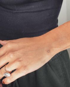 a woman's hand with a small tattoo on her left wrist, and a diamond ring in the middle