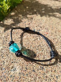 Torch made by hand, one at a time, a teal green with sparkling dichroic lampwork glass bead tied into a black leather cord adjustable length sliding barrel knot bracelet. Adjustable Leather Bracelet With Round Beads As Gift, Adjustable Leather Bracelet With Round Beads For Gift, Adjustable Glass Jewelry With Cord, Adjustable Cord Glass Jewelry, Adjustable Turquoise Glass Bracelets, Adjustable Green Leather Bracelet As A Gift, Festival Armband, Barrel Knot, Climbing Outfits