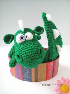 a crocheted green stuffed animal sitting in a box with a flower on the side